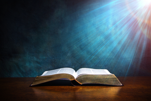 Dramatically lit open bible sits atop wooden table
