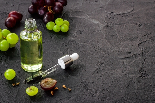 Grapes sit next to clear bottle of grapeseed oil and dropper