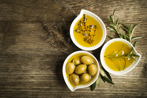 Three ramekins of olive oil with olives and herbs sit next to each other