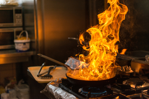 A pan of burning olive oil with tall flames sits atop a stove
